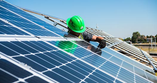 A worker installs photovoltaic panels in a large outdoor solar array.