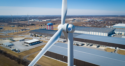 A wind turbine operates in the foreground, surrounded by a small town.