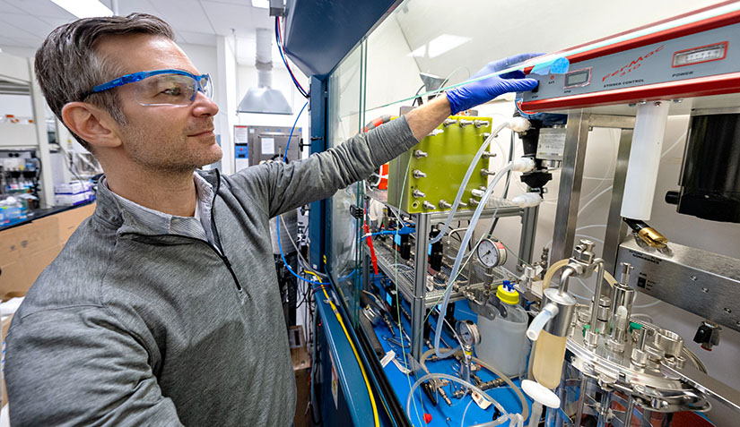 One researcher with safety glasses working in equipment in a lab.