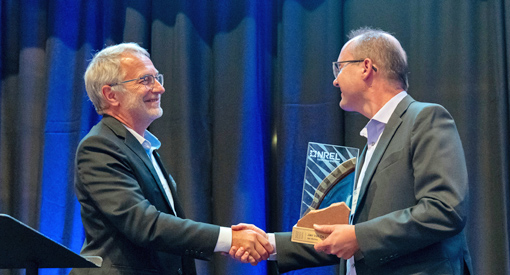 Two people shake hands, one of whom holds a plaque.