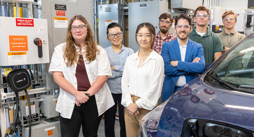 Seven people pose alongside a vehicle in a laboratory.