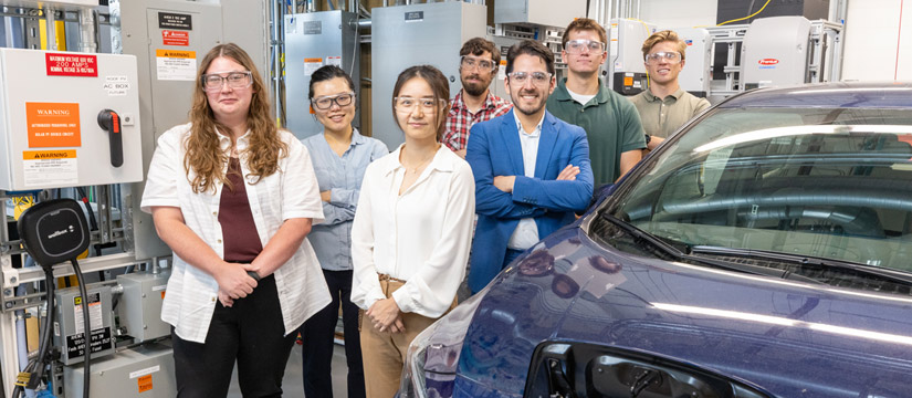 Seven people pose alongside a vehicle in a laboratory.