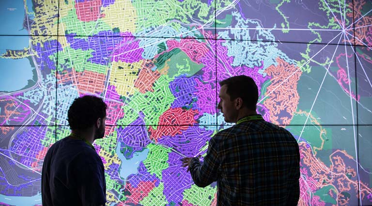 Two people discuss a map projected onto a wall