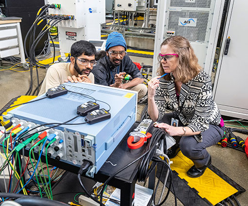 Three people work on electrical system inside laboratory.