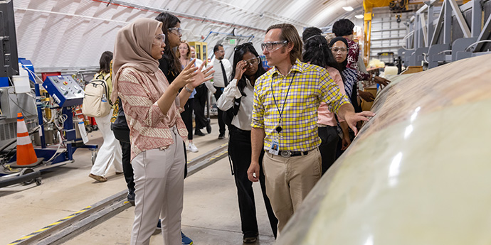 Two people have a conversation in a laboratory with a small group of people in the background.