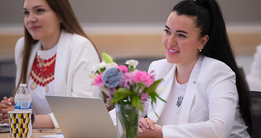 Two people sit at desk listening to presentation.