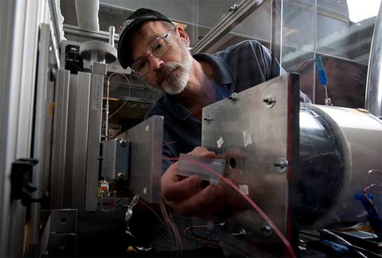 Photo of a man adjusting equipment in a lab, specifically an air-cooling test bench.