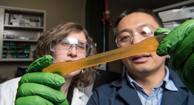 A researcher holds a long, translucent, orange resin