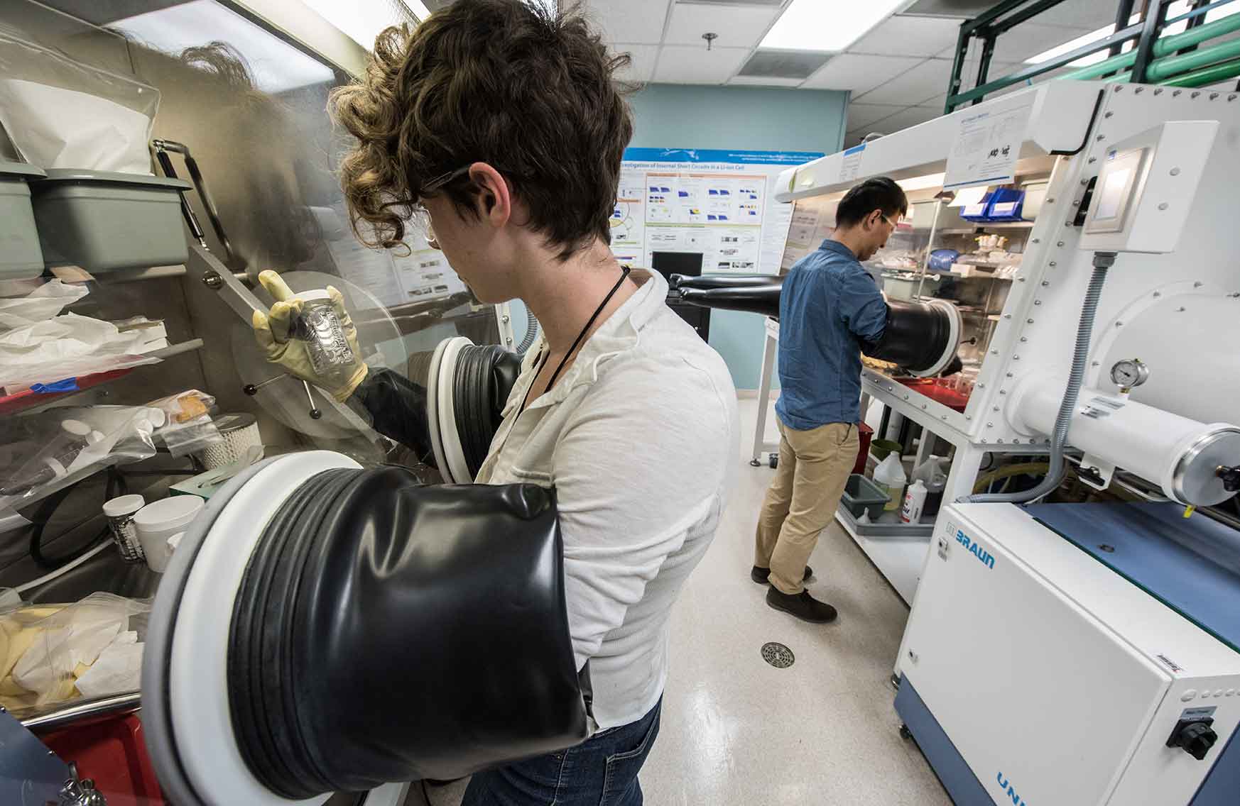 Two researchers using glove boxes in energy storage laboratory.