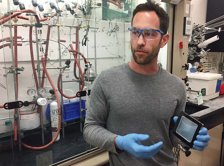 Photo shows a man in a laboratory holding a small square of glass.