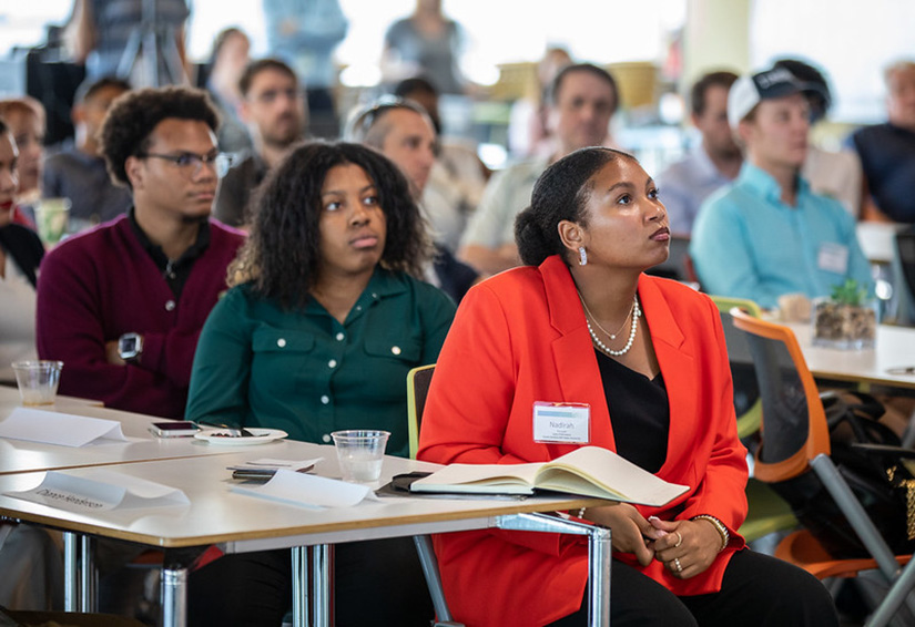 Three people sitting at a table in a large room full of other people at NREL.