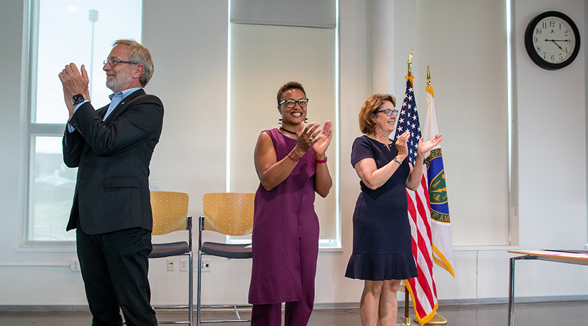 Three people standing and clapping hands at NREL.