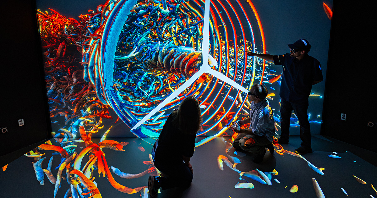 three researchers in silhouette interacting with a multicolor 3D visualization featuring a wind turbine.