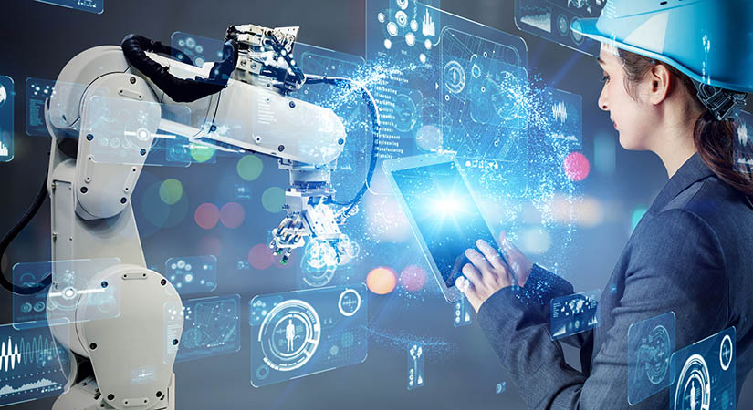 A worker in a hard hat referencing a computer pad, and working near a robotic arm against a background overlain with digital visuals