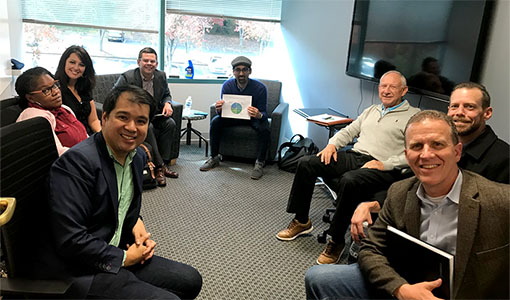 Eight people sit in a circle, smiling toward the camera.