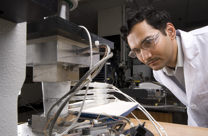 A person wearing safety goggles examines machinery in a lab.