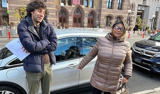 Two people stand in front of an electric vehicle.