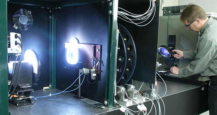 Spectral responsivity measurement system using 10nm bandwidth interference filters. L to R, lamp, mechanical chopper, shutter, filters, temperature controlled probe station with mirror.