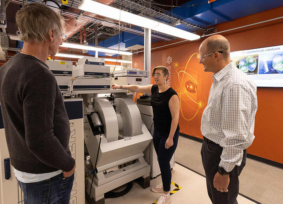 A group of researchers talking and standing next to a machine.