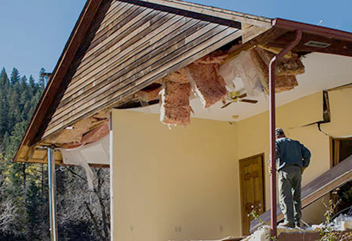 A person stands in the frame of a damaged home