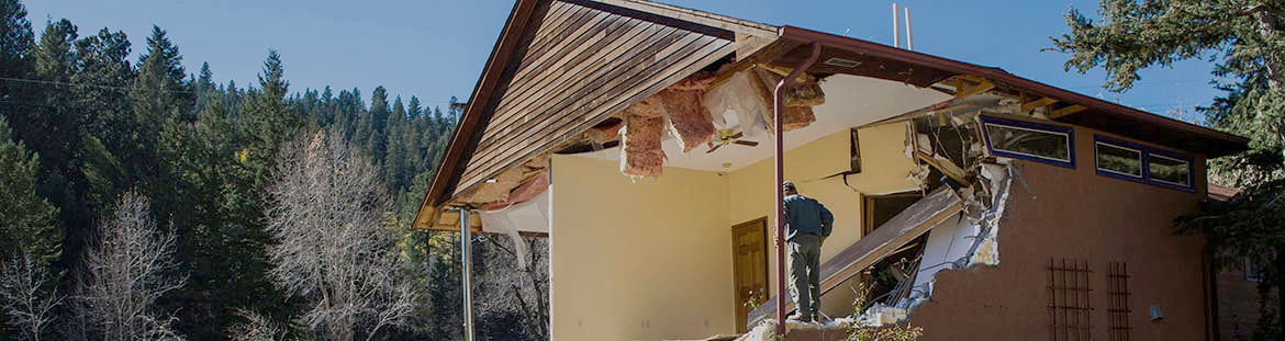 A person stands in the frame of a damaged home