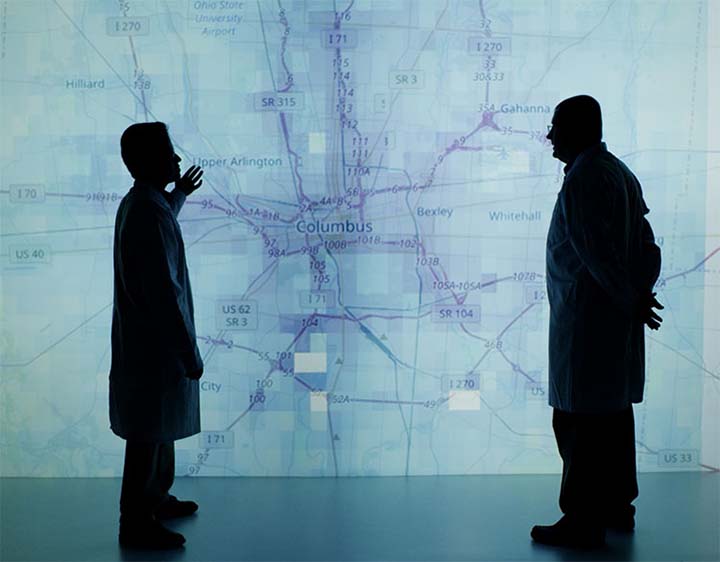 Two researchers stand in front of a blue-green raod map of Columbus, Ohio, in NREL's visualization room.