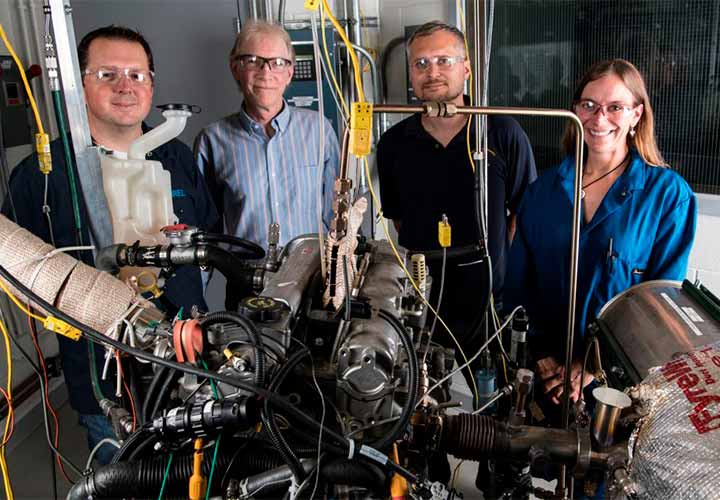 Four people standing by scientific equipment in laboratory setting