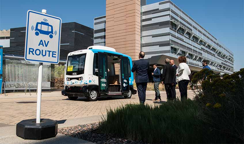 Photo of people standing next to a 12-passenger automated vehicle.