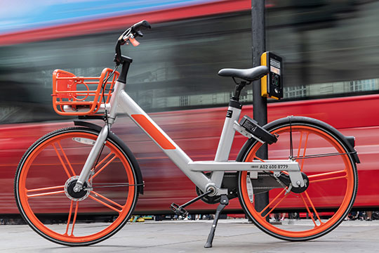 An electric bicycle parked in front of a moving rail car.