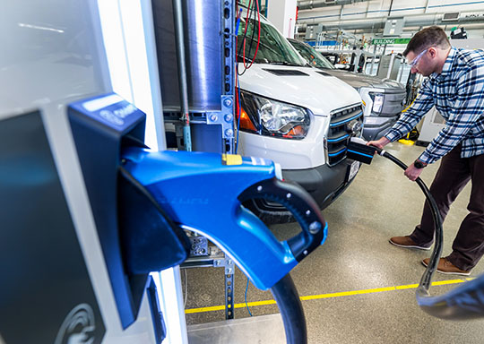 A person plugging a charger into an electric vehicle, with another charger in a charging port in the foreground.