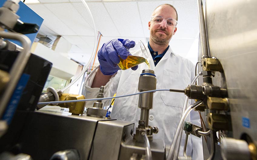 A researcher in a lab pours fuel into an ignition quality tester.