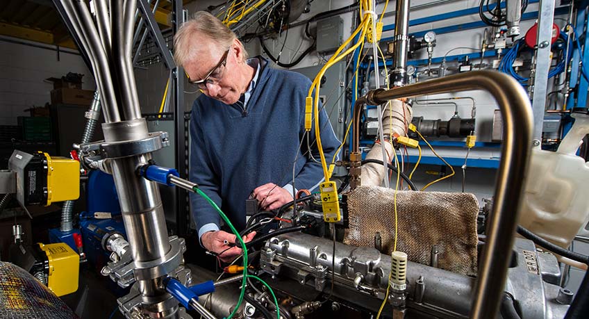 A researcher works on a 4-cylinder spark ignition engine that was converted into a single-cylinder engine for research purposes.