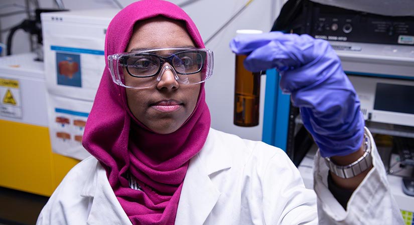 A woman in a lab holding a test tube in the air.