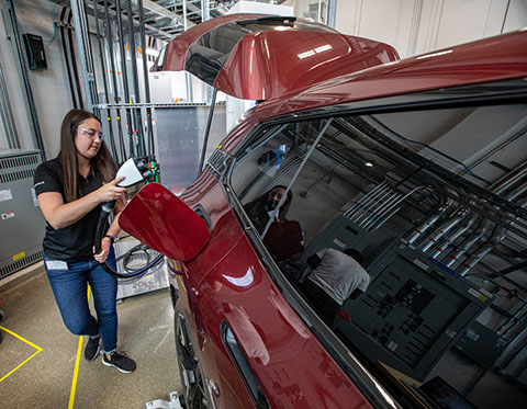 A woman plugs a charger into a red electric vehicle.