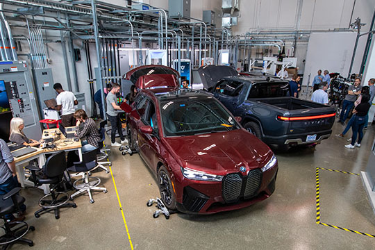 Researchers sit at computer desks and stand around two EVs in an ESIF lab.