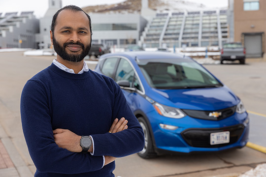 Ranjit Desai, smiling with arms folded in front of a parked light-duty passenger EV.