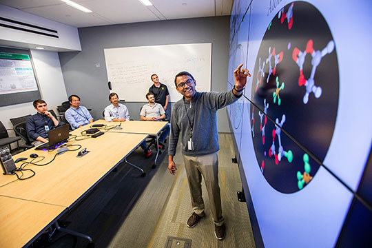 A researcher pointing to a projected image and talking to others seated around a table.