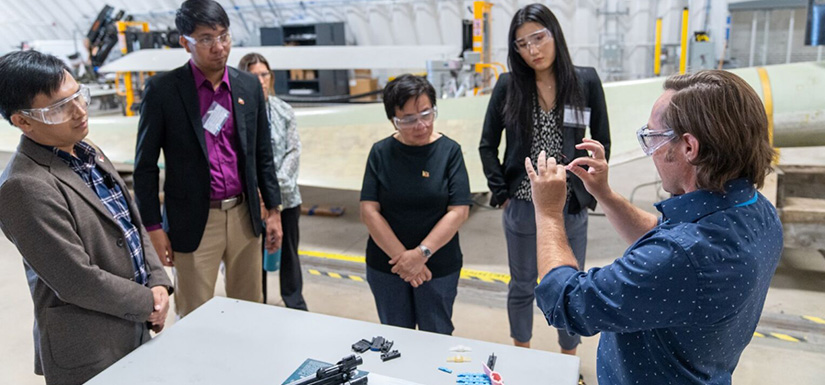 Group of people inside laboratory looking at small wind turbine pieces.