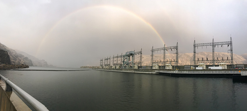 Photo of a hydropower dam with a rainbow in the background.