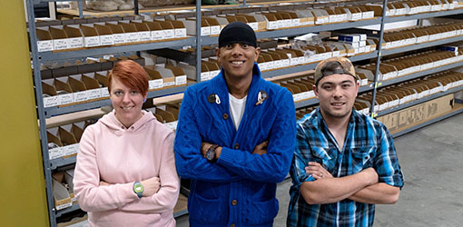 Three people stand in front of stocked shelves.